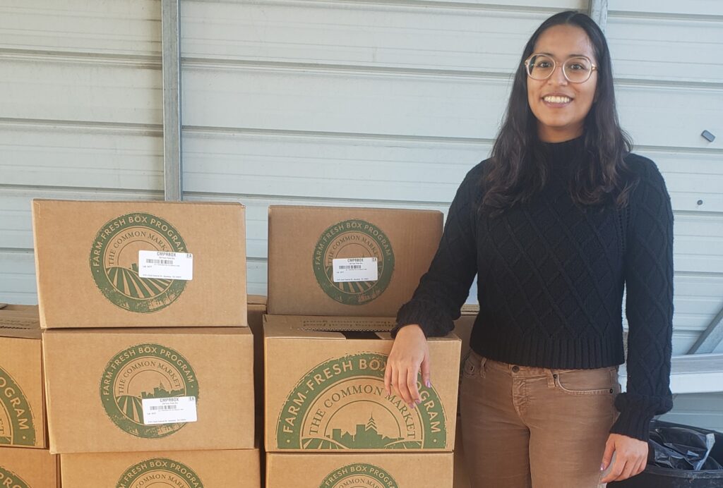 Tiffany stands with stacked produce boxes for the Neighborhood Produce Program.
